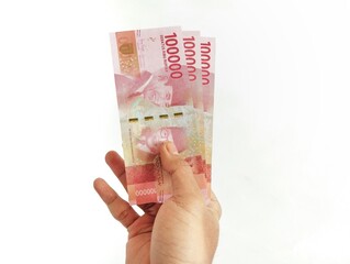 Hand holding Indonesian Rupiah banknotes against a clean white background for financial...