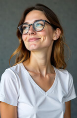 Fototapeta premium smiling woman in white t-shirt and glasses looking away. casual and confident expression against gray background. portrait photography, lifestyle, fashion
