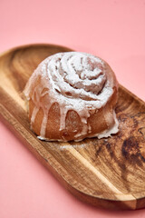 Delicious sugar-dusted cinnamon roll on wooden tray against pink background