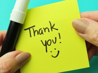 Woman hands holding a pen and a yellow stick note with the handwritten expression 