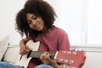 Music, woman and playing guitar for song. African American woman playing guitar on sofa in living...