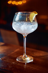 Chilled cocktail with lemon garnish in elegant wine glass on wooden bar