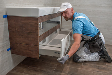 Installation of bathroom furniture. The plumber inserting a drawer into a washbasin cabinet.