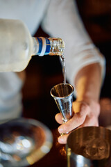 Pouring vodka into jigger with precision in a dimly lit bar setting
