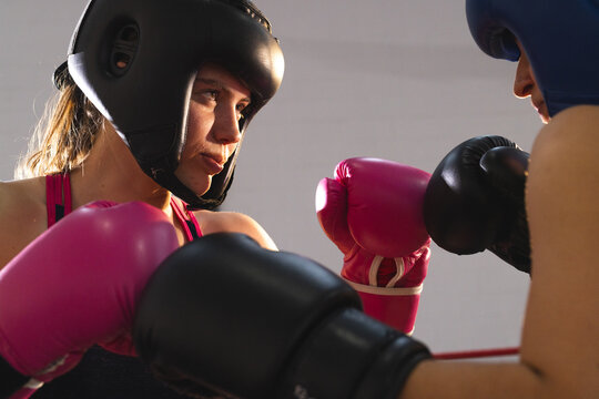 Female boxer wearing pink gloves and black headgear sparring with opponent in ring with red ropes