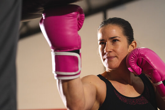 Female athlete punching toward camera in gym wearing sleeveless top, pink boxing gloves, copy space