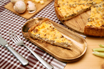 Savory mushroom and cheese quiche slice on wooden plate with checked tablecloth