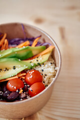 Healthy vegan bowl with avocado cherry tomatoes and quinoa on wooden table setting