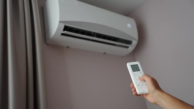 Man holds air conditioner remote control and sets cooling temperature of split system to 17 degrees. Concept of air cooling, comfortable temperature in heat in room, climate control