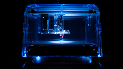 Close up of a transparent blue 3d printer with its nozzle extruding filament in a dark futuristic environment with dramatic lighting