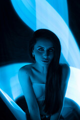 woman poses against a backdrop of swirling blue light, highlighting her features and creating an...