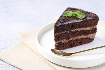 Piece of delicious chocolate cake with mint and spoon on grey table, closeup