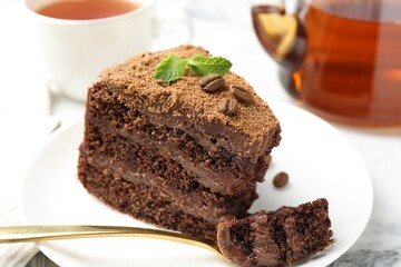 Piece of delicious chocolate cake with coffee beans, mint and fork on white marble table, closeup