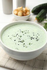 Tasty cucumber soup, croutons and ingredients on white wooden table, closeup