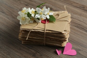 Stack of love letters, paper hearts and flowers on wooden table, closeup