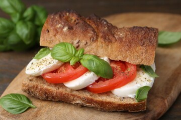 Tasty sandwich with mozzarella cheese, tomatoes and basil on wooden table, closeup