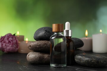 Spa composition with wet stones, cosmetic products and burning candles on dark table against blurred green background, selective focus