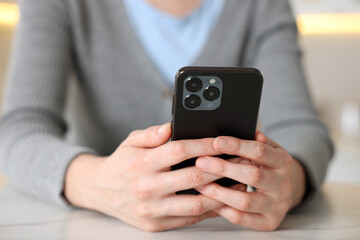 Woman using smartphone at table indoors, closeup