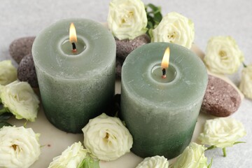 Burning candles, stones and rose flowers on light grey table, closeup