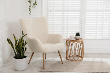 Comfortable armchair, side table and houseplants near white wall indoors