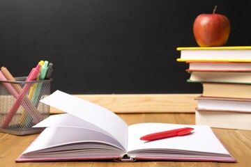 Different stationery and apple on wooden table near blackboard, closeup