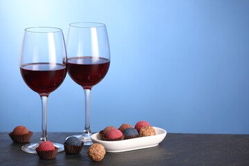 Delicious truffle bonbons and wine on black table against blue background. Space for text