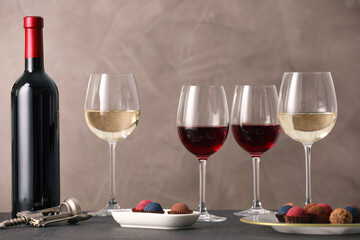 Delicious truffle bonbons and wine on black table against grey background