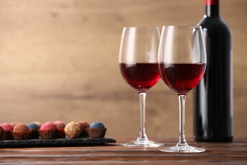 Delicious truffle bonbons and wine on wooden table. Space for text