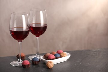 Delicious truffle bonbons and wine on black table against grey background. Space for text
