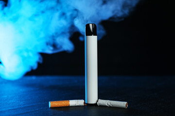Electronic smoking device and broken cigarette on black table in blue light