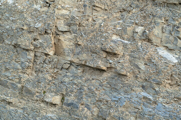 Texture, background layers and cracks in sedimentary rock on cliff face. Cliff of rock mountain. Wild stone protruding crumbling layered blocks.
