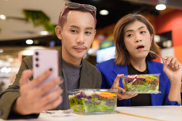 Gender diverse coworker business team eating salad and working digitally taking selfie with phone