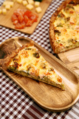 Savory quiche slice with broccoli and cheese on wooden plate checkered tablecloth