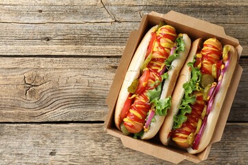 Tasty hot dogs with vegetables, mustard and ketchup on wooden table, top view. Space for text