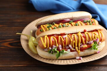 Delicious hot dogs with sauces, lettuce and onion on wooden table, closeup