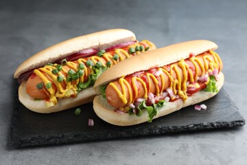Delicious hot dogs with sauces, lettuce and onion on grey textured table, closeup