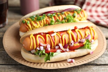 Delicious hot dogs with sauces, lettuce and onion on wooden table, closeup