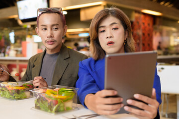 Gender diverse coworker business team eating salad and working digitally