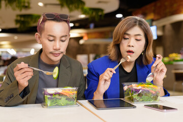 Gender diverse coworker business team eating salad and working digitally
