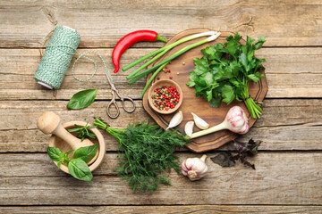 Different fresh herbs, spices, scissors, thread, mortar and pestle on wooden table, flat lay