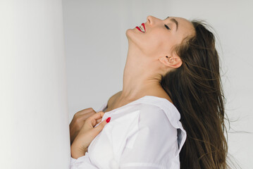 a beautiful sexy girl in a white men's shirt poses near a wall background