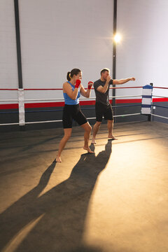 Male and female athletes practicing jabs in boxing ring wearing red hand wraps under spotlight