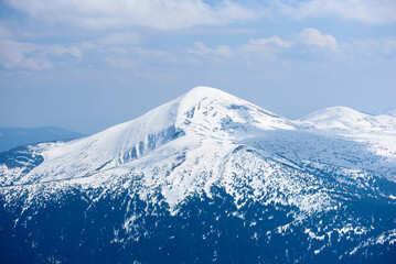 Snow-covered mountain peak under clear blue sky, with patches of snow on slopes and scattered...