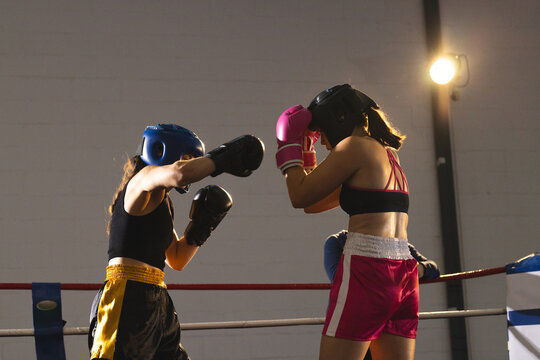 Female athletes sparring in boxing ring, wearing headgear and gloves near red, white and blue ropes