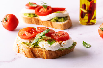 Fresh homemade caprese sandwich with avocado paste, mozzarella cheese, cherry tomatoes, fresh aromatic basil leaves and spicy hot oil close up. Healthy homemade food concept.