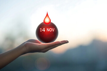 Hand holding a red sphere with 14 N O V text and a blood drop against a blurred background
