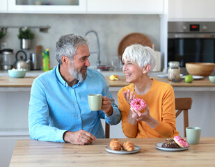 A man and a woman are smiling and holding cups of coffee in a kitchen. Scene is happy and friendly
