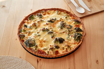 Savory broccoli quiche with cheese topping on wooden table setting
