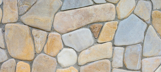 Stone masonry with multi-colored, smooth boulders creates a unique texture. Natural shades of gray, beige, and brown stones fit tightly together, forming a strong and aesthetically pleasing surface.