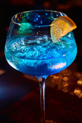 Luminous blue cocktail in goblet glass with lemon slice and ice cubes